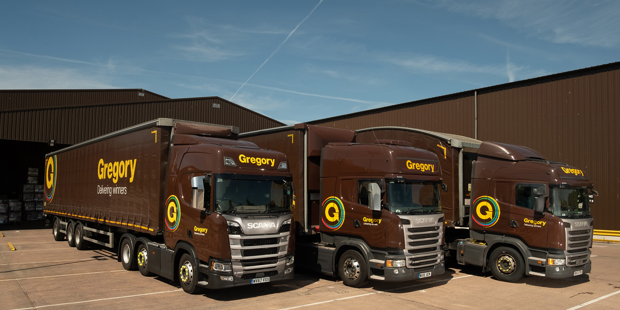 Three Gregory trucks lined up outside of warehouse.